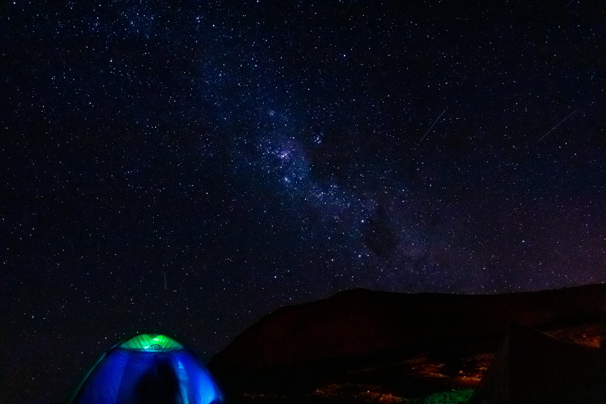 Cielo estrellado sobre una carpa iluminada y montañas oscuras
