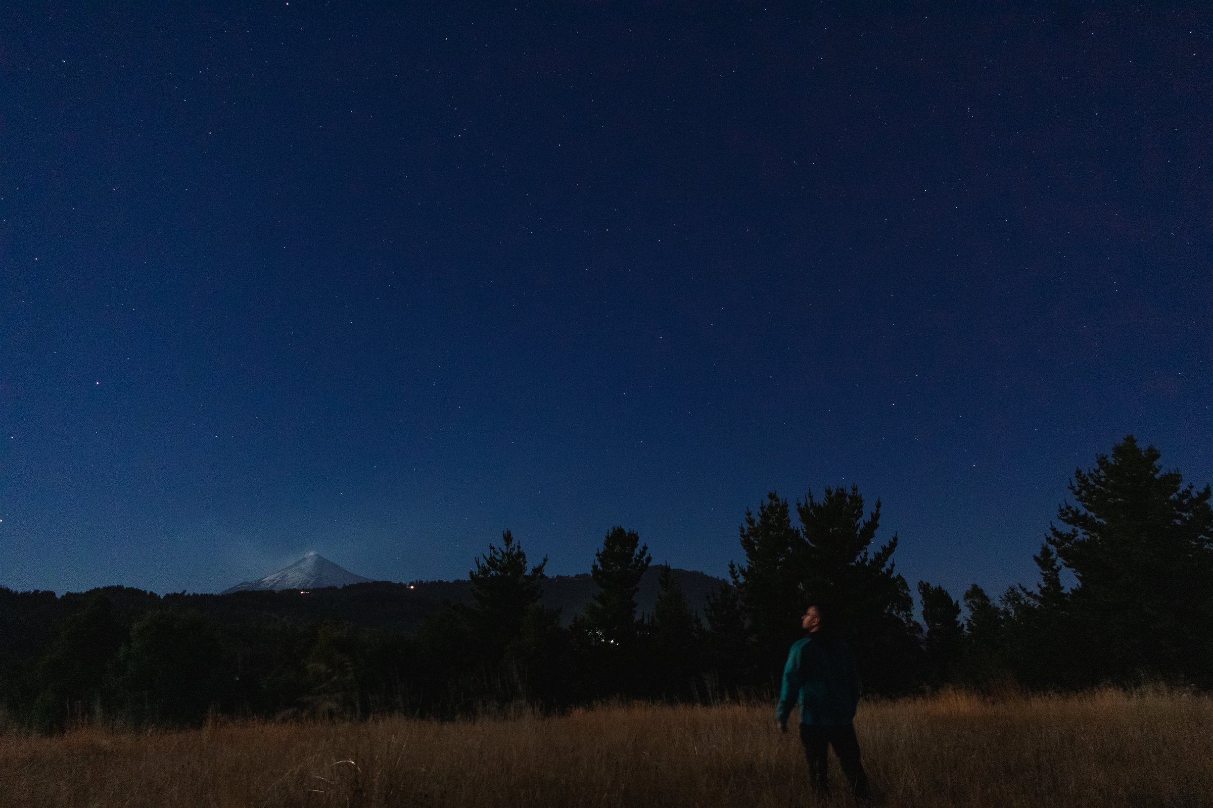 Persona observando un cielo estrellado frente a un volcán